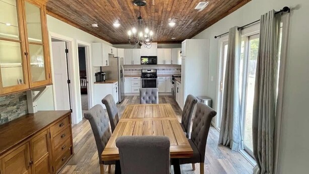 Un comedor con una mesa y sillas de madera, una cocina al fondo y un techo de madera.