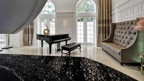 Une grande pièce avec un piano, un canapé et une grande fenêtre avec des rideaux.