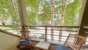 Un balcón con dos sillas de madera y una pequeña mesa, con vistas a una calle con árboles y edificios.