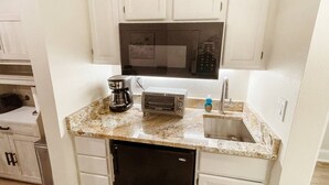 Cocina compacta con armarios blancos, microondas, tostadora, cafetera y lavavajillas.