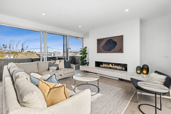 A modern living room with a sofa, coffee table, fireplace, and large windows.