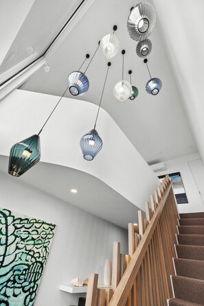 A modern interior with a staircase, pendant lights, and a large abstract painting.
