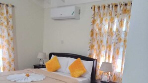 Un dormitorio con una cama, dos almohadas, una mesita de noche, una lámpara y cortinas.