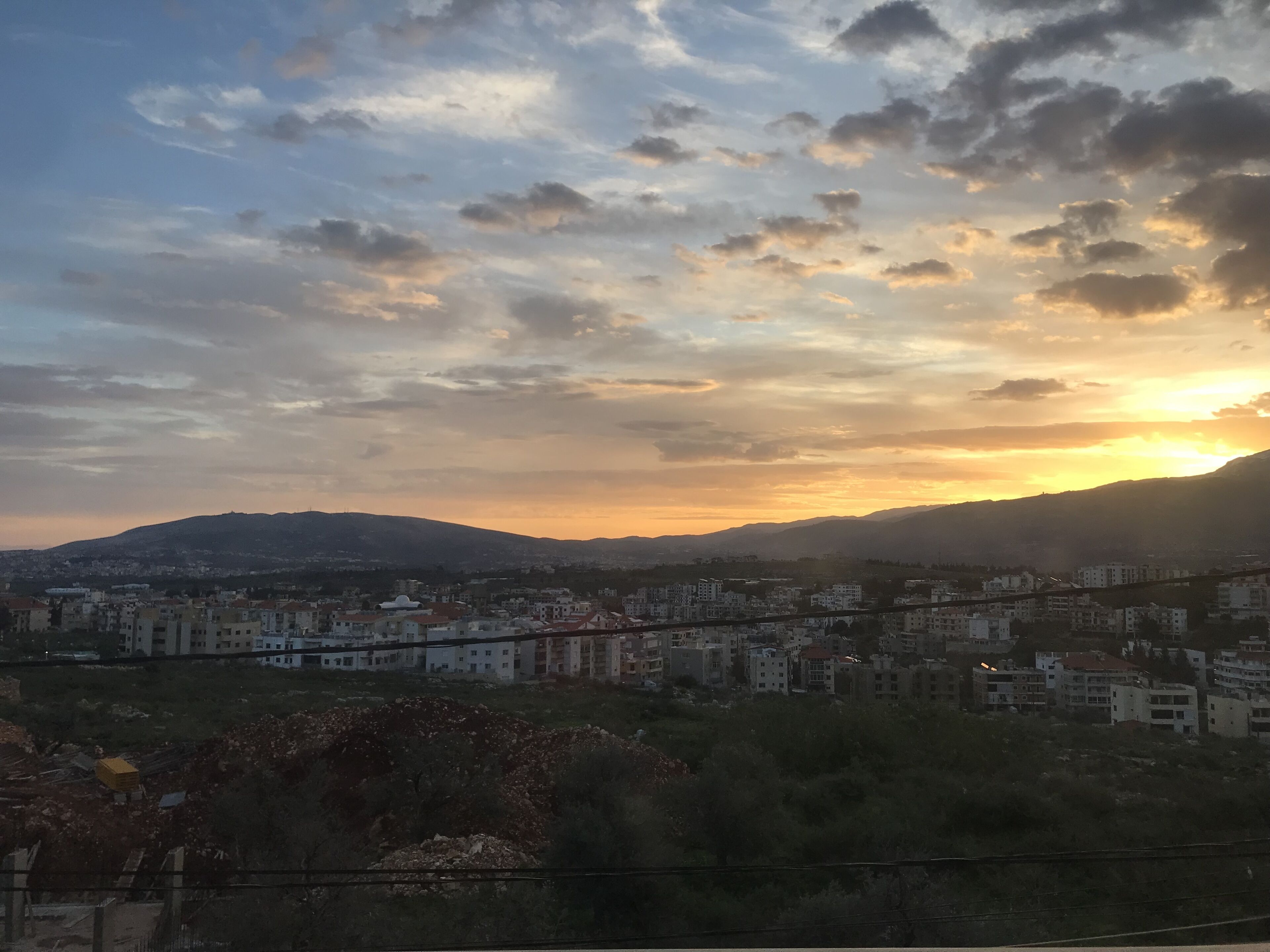A cityscape with a sunset over mountains, featuring residential buildings and a church.