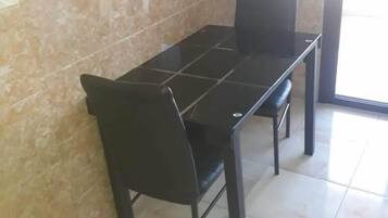 A dining area with a black table and chairs, a tiled floor, and a marble wall.