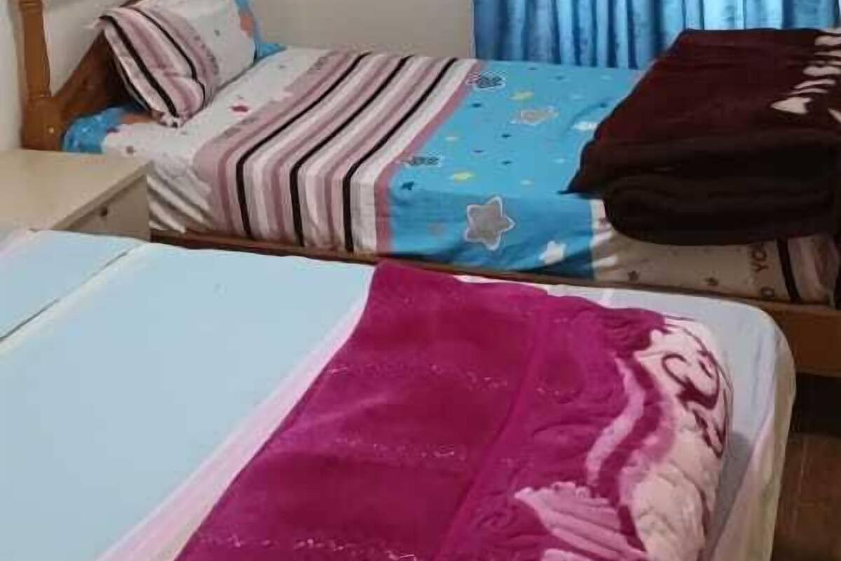 A bedroom with two beds, a wooden headboard, a blue curtain, and a bedside table.