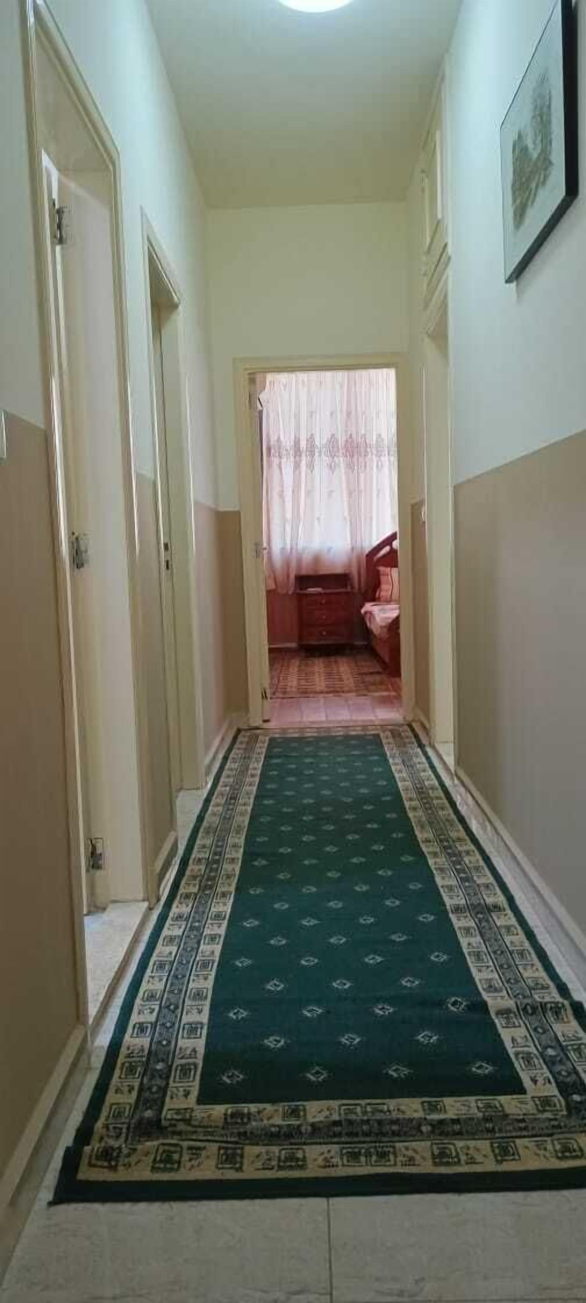 A hallway with a patterned carpet, a door on the left, and a bed in the distance.