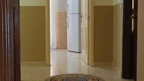 Un pasillo con felpudo, un refrigerador y una puerta que da a otra habitación.