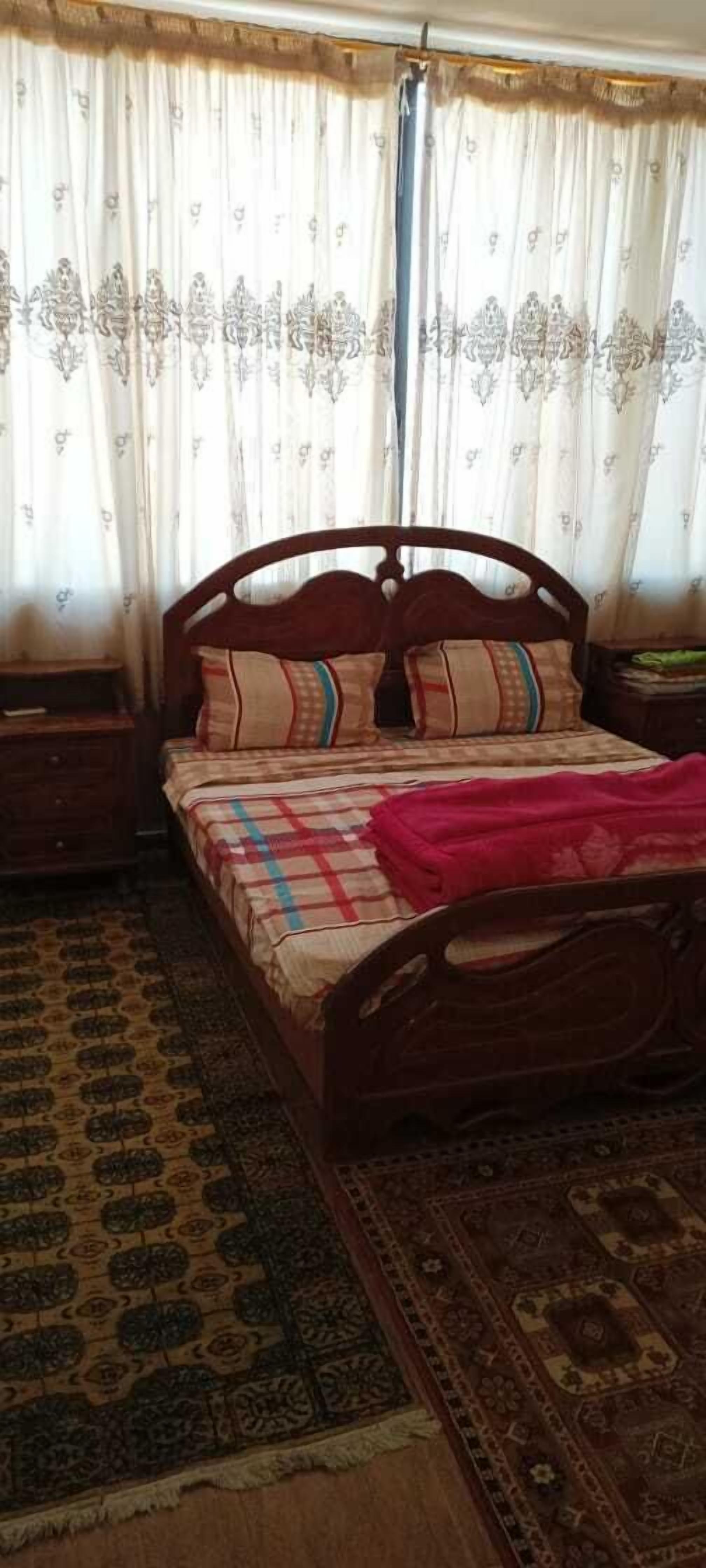 Un dormitorio con una cama de madera, cortinas estampadas y una alfombra tradicional.