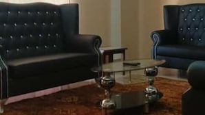 Una sala de estar con dos sofás negros, un tapete estampado, una mesa de centro y una lámpara de techo.