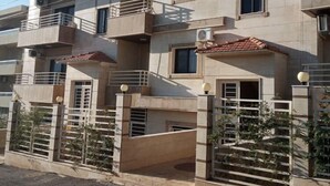 Un edificio residencial de varios pisos con balcones, unidades de aire acondicionado y una entrada protegida por un portón.