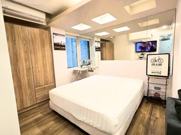 Une chambre d’hôtel moderne, dotée d’un grand lit, d’une armoire, d’une coiffeuse avec un miroir, d’une petite table et d’un téléviseur.