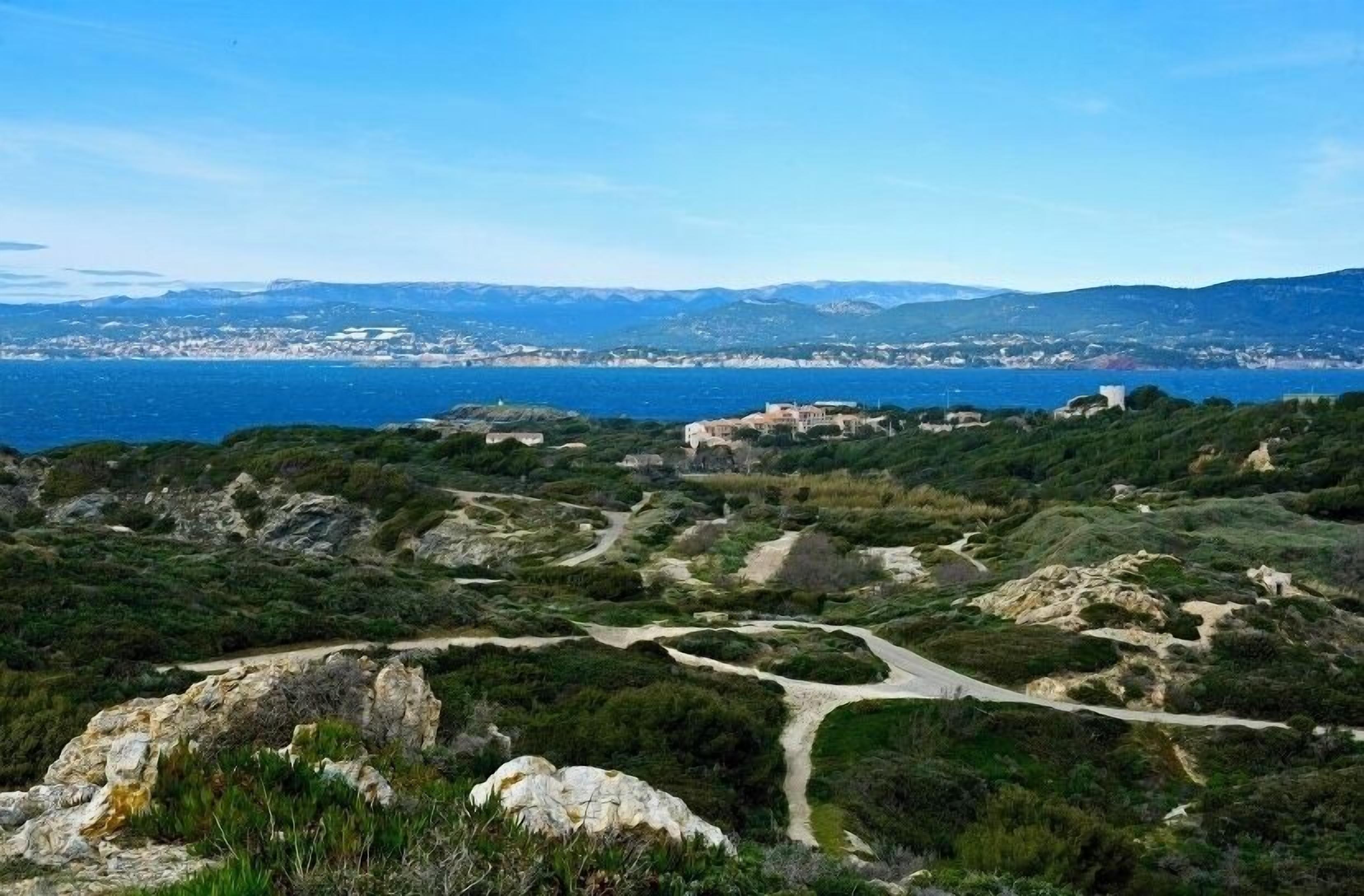 A coastal landscape with a winding road, rocky terrain, and buildings in the distance.