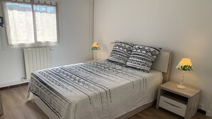 Une chambre à coucher avec un grand lit, deux tables de chevet avec des lampes, un radiateur et une fenêtre avec des rideaux.