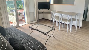 Un salon comprenant un canapé, un téléviseur, une table à manger avec des chaises et un coin cuisine.