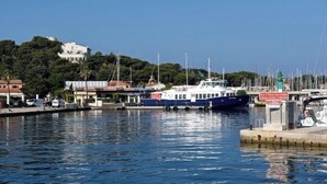 Un port de plaisance avec des bateaux amarrés, un bâtiment blanc sur une colline et un panneau indicateur.
