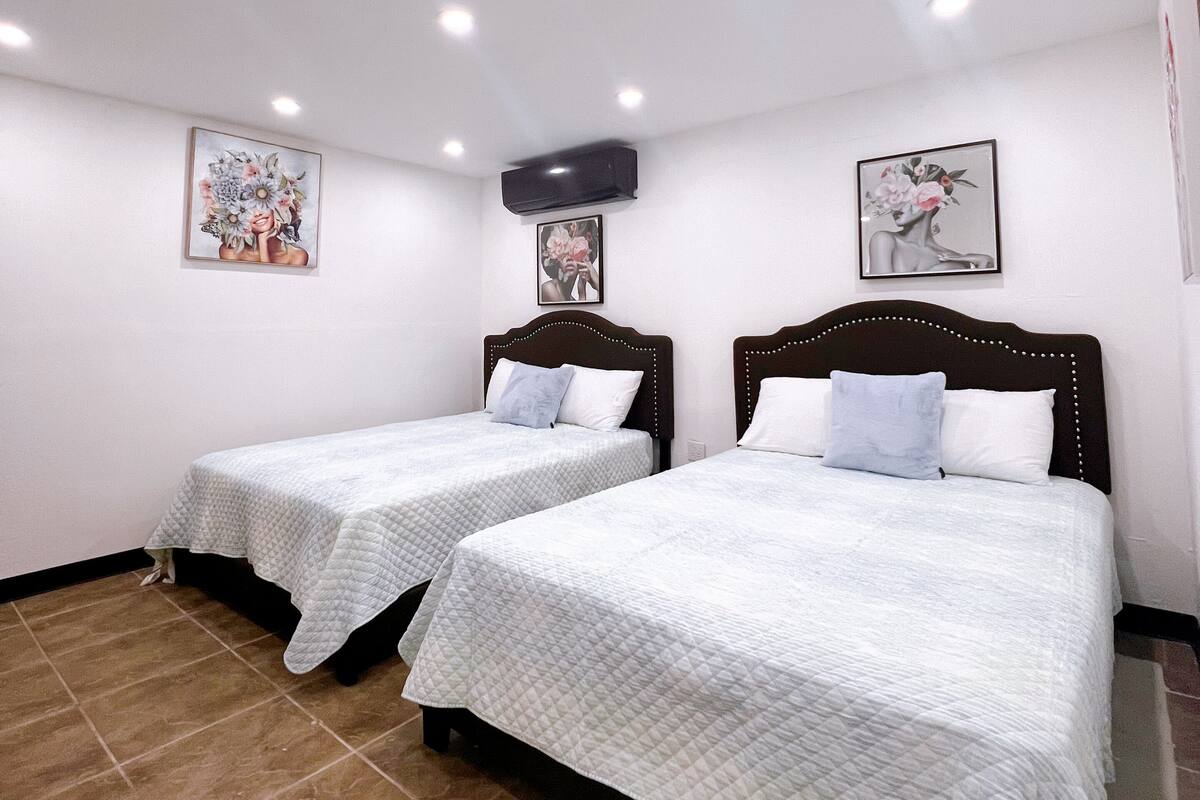 Une chambre d’hôtel avec deux lits, un climatiseur au plafond et des œuvres d’art accrochées aux murs.