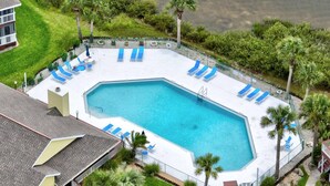 An aerial view of a swimming pool surrounded by blue lounge chairs, a small deck area, and palm trees. - New Intracoastal Oasis | Flagler Beach | Intracoastal Views | Walk To The Beach | Solar Heated Pool (Flagler Beach)