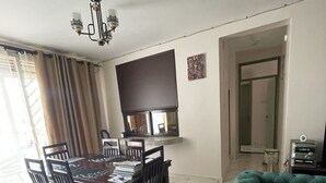 A dining area with a table and chairs, a television mounted on the wall, a green sofa, and a tiled floor. - Fully-furnished 2BR/2BA Condo in Kampala with WiFi, gym, pool, Gated Community (Kampala)