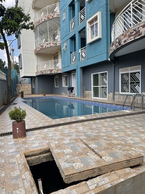A residential building with a swimming pool, balconies with metal railings, and a small garden area. - Fully-furnished 2BR/2BA Condo in Kampala with WiFi, gym, pool, Gated Community (Kampala)