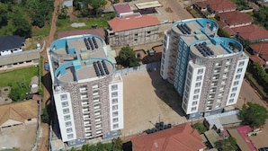 A high-rise building with a central courtyard, surrounded by smaller buildings and greenery. - Fully-furnished 2BR/2BA Condo in Kampala with WiFi, gym, pool, Gated Community (Kampala)