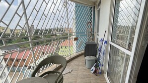 A balcony with wicker furniture, a view of the city, and a window with blinds. - Fully-furnished 2BR/2BA Condo in Kampala with WiFi, gym, pool, Gated Community (Kampala)