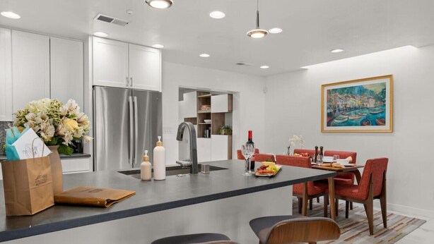 A modern kitchen with a central island, stainless steel appliances, and a dining area with red chairs and a table set for two. - Modern & Cozy Santa Fe Escape (Santa Fe)