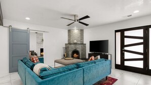 A modern living room with a blue sectional sofa, a fireplace, a flat-screen TV, and a large sliding glass door. - Modern & Cozy Santa Fe Escape (Santa Fe)