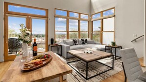 Ein geräumiges Wohnzimmer mit großem Fenster, einer Couch, einem Couchtisch und einem Essbereich mit Holztisch, gedeckt für eine Mahlzeit.