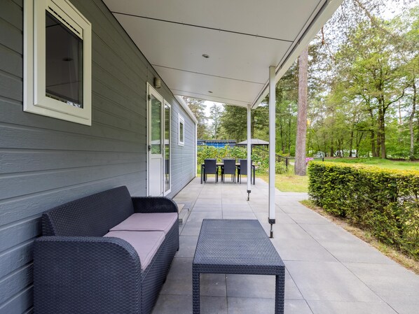 A covered patio with a sofa and table, a covered outdoor area, and a view of a garden and trees.