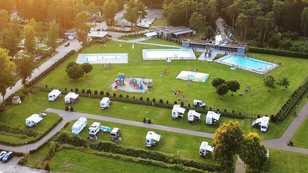 An aerial view of a campground with multiple RVs, a swimming pool, and a playground. - chalet with covered terrace on campsite with pool (Vessem)
