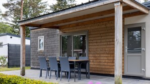 A covered outdoor seating area with a table and chairs, a wooden wall, and a door with a number 589 sign. - chalet with covered terrace on campsite with pool (Vessem)
