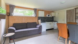 A compact living space with a sofa, a small table, a kitchenette, and a dining area. - chalet with covered terrace on campsite with pool (Vessem)