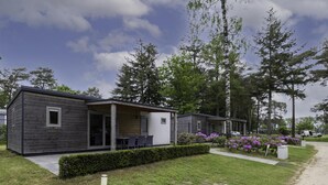 A modern mobile home with a patio area, surrounded by greenery and trees. - chalet with covered terrace on campsite with pool (Vessem)