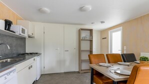 A compact kitchen with a stove, microwave, and sink. There is a dining area with a table and chairs. - Chalet on park with many facilities and pool (Vessem)