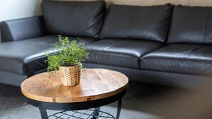 A modern living room with a leather sofa, a round wooden coffee table with a woven plant holder, and a metal wireframe base. - Chalet on park with many facilities and pool (Vessem)