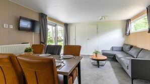 A modern living room with a dining area, leather furniture, a flat-screen TV, and large windows. - Chalet on park with many facilities and pool (Vessem)