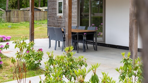 A covered patio area with a wooden table and chairs, a sliding glass door, and a number 588 sign. - Chalet on park with many facilities and pool (Vessem)