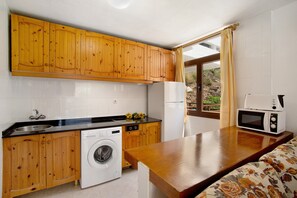 Une cuisine compacte avec des meubles en bois, un lave-linge, un four à micro-ondes et une fenêtre avec des rideaux.