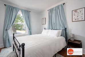 A bedroom with a bed, curtains, a nightstand, and a window. - Holland Hideaway (Holland)