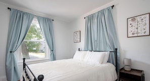 A bedroom with a bed, curtains, a nightstand, and a window.