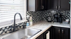 Una cocina moderna con un lavamanos de acero inoxidable, armarios negros y un salpicadero de azulejos.