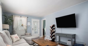 A living room with a sofa, a coffee table, a bookshelf, and a TV mounted on the wall. - Holland Hideaway (Holland)