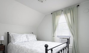 A bedroom with a bed, a nightstand, a lamp, and a window with curtains.
