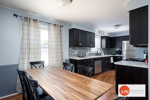 A modern kitchen with dark cabinets, a marble countertop, and a wooden dining table with chairs. - Holland Hideaway (Holland)
