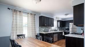 A modern kitchen with dark cabinets, a marble countertop, and a wooden dining table with chairs. - Holland Hideaway (Holland)