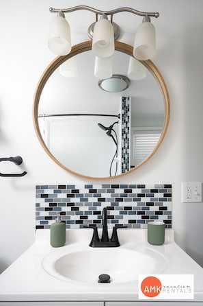 A bathroom with a round mirror, a white sink, and a tiled backsplash. - Holland Hideaway (Holland)