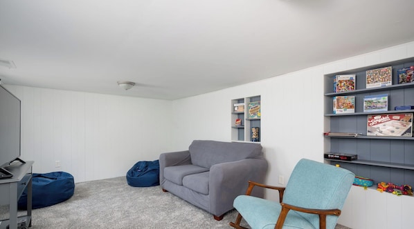 A room with a grey sofa, blue bean bag, and a rocking chair. There are shelves with board games and a desk with a computer.