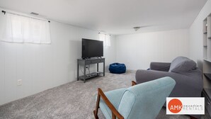 Una habitación moderna y minimalista con una televisión sobre un mueble bajo, un sillón de saco y un sofá gris.