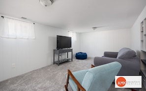 A modern, sparsely furnished room with a television on a stand, a bean bag, and a grey sofa.